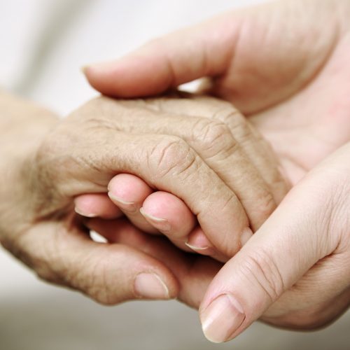 An elderly hand held by young hands