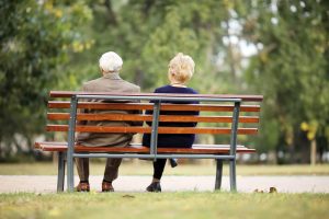 Rear view of a senior couple sitting outdoor on bench.