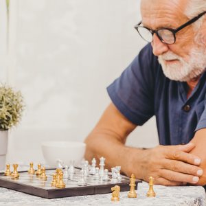 Elderly man playing Chess board game at home for training brain