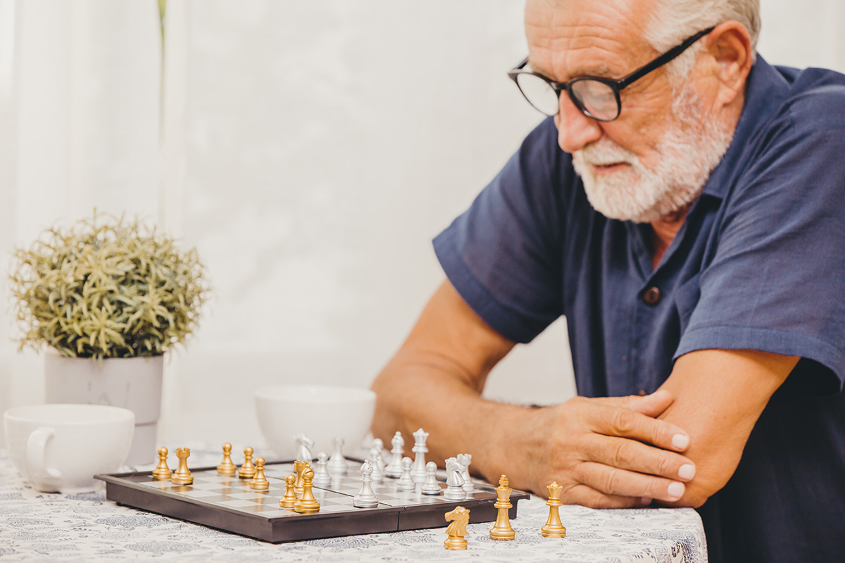Elderly man playing Chess board game at home for training brain