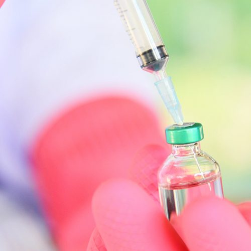 A vaccination being prepared with medication being drawn from a syringe.