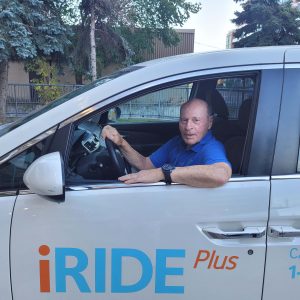 Sheldon, a Circle of Care iRIDE driver, sits in an iRIDE vehicle and smiles at the camera.